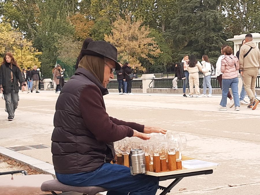 M&uacute;sico tocando un arpa de cristal formada por copas de vino afinadas con agua, frotando los bordes con los dedos mojados en el parque de El Retiro, Madrid
