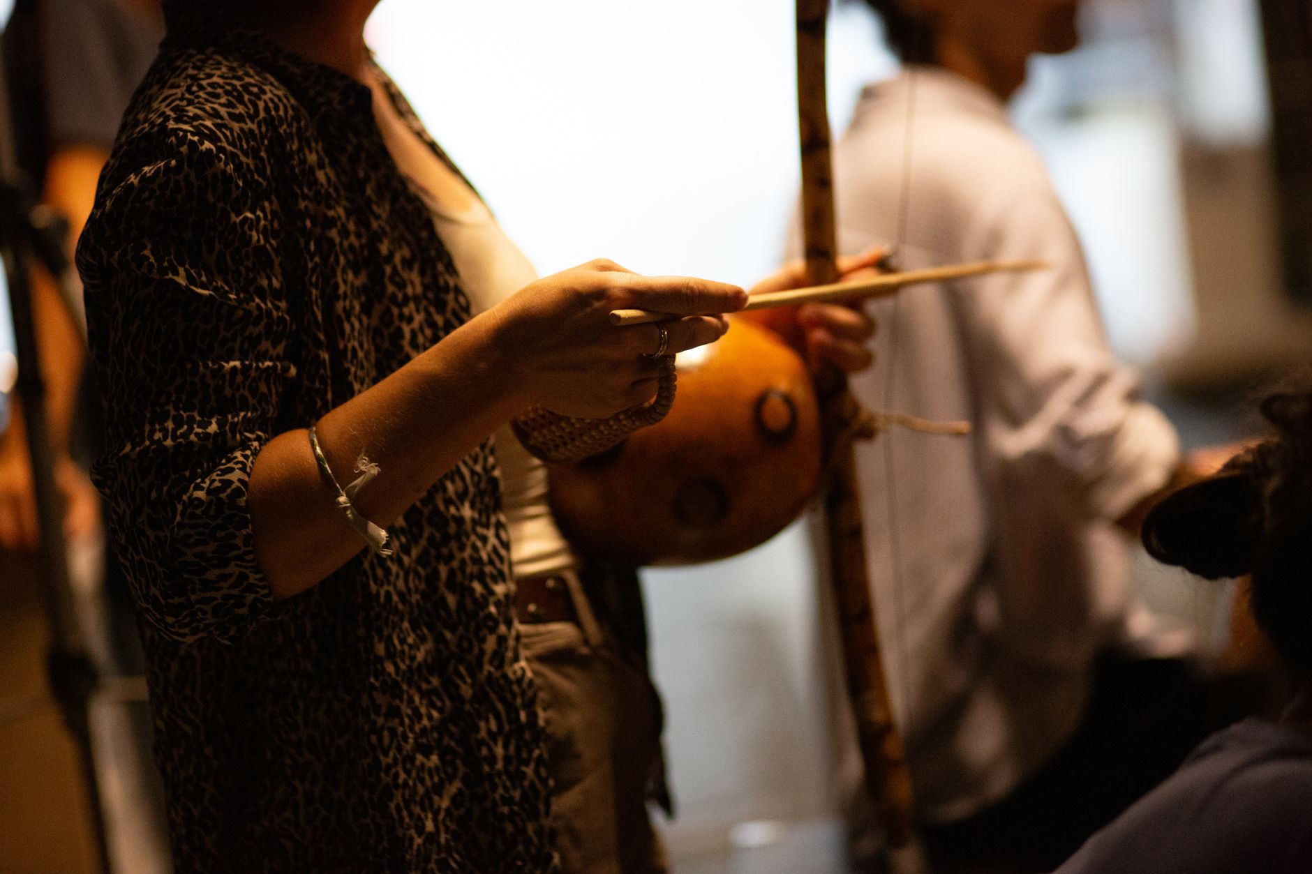 Mano sujetando la baqueta y golpeando la cuerda del berimbau junto a la cabaza de resonancia